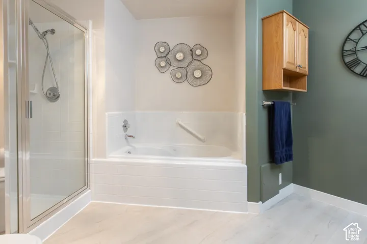 Glass-enclosed shower, built-in soaking tub, light wood-finish flooring, wall-mounted wooden cabinet, and a towel bar