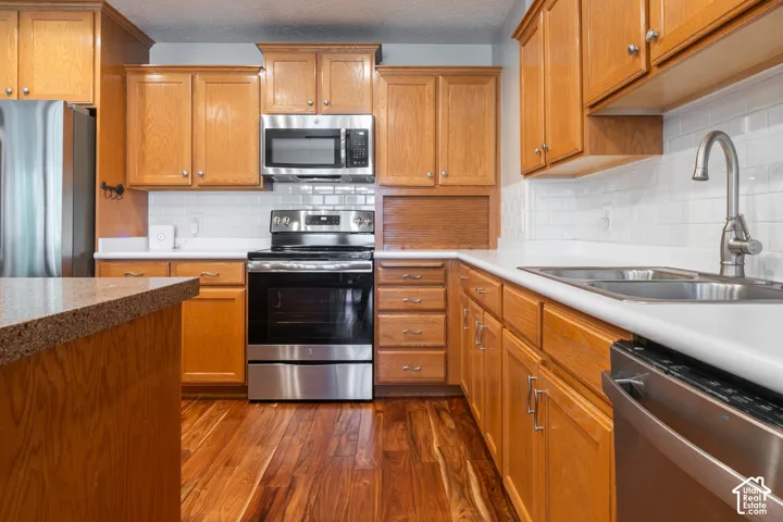 Kitchen featuring wood-finish flooring, light wood cabinetry, stainless steel appliances, white subway tile backsplash, and a double basin sink with a high-arc faucet