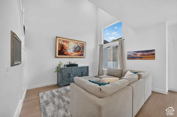 Vaulted ceiling with a high window, light wood-finish flooring, and white wall finishes