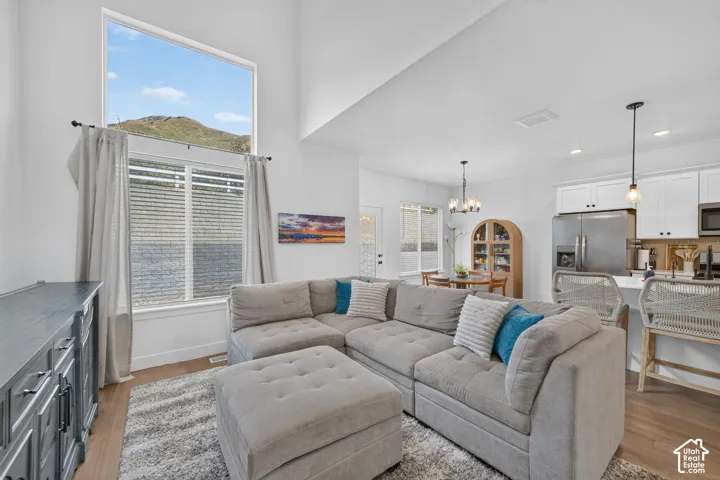 Vaulted ceiling with a large fixed window, wood-finish flooring, white cabinetry, stainless steel appliances, and a kitchen island with seating