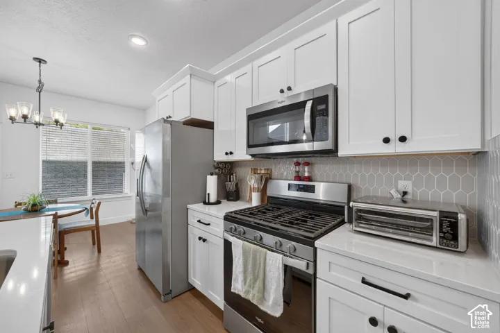 White shaker cabinetry, stainless steel appliances, light wood-finish flooring, light countertop, and a gray geometric tile backsplash