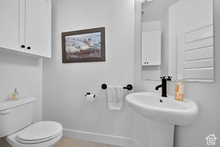 Clean and bright bathroom featuring a pedestal sink with matte black fixtures, white cabinetry with ample storage, a toilet with elongated bowl, and neutral tile flooring
