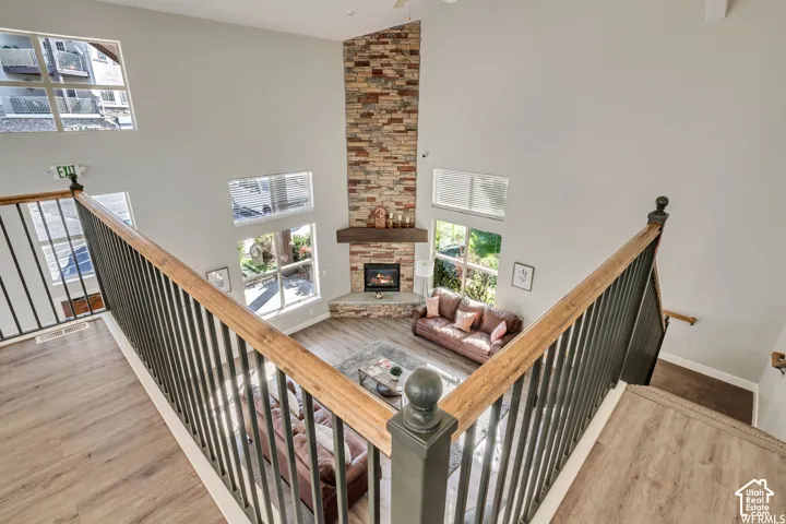 Two-story living area featuring a stone accent wall, wood-finish flooring, multiple windows, and a corner fireplace with a wood mantel