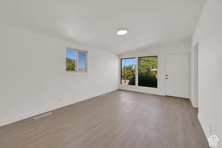 Wood-finish flooring, white walls, multiple windows, recessed lighting, and a white entry door