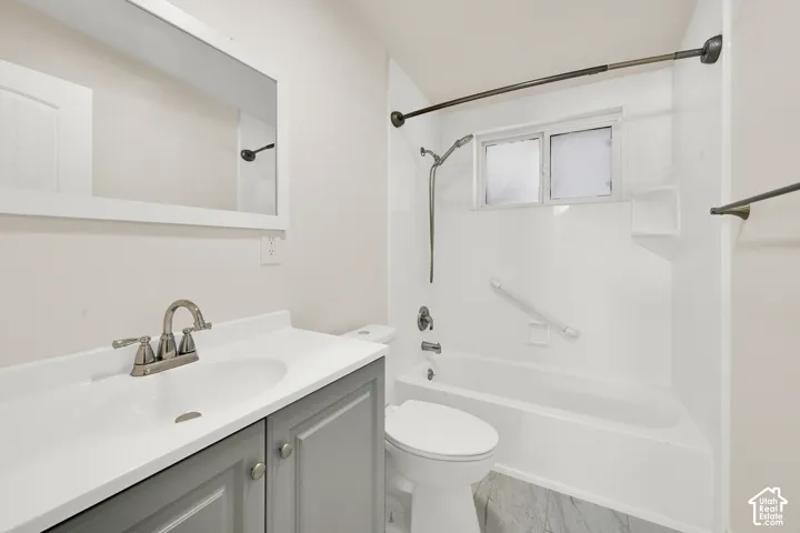 White vanity with a single basin sink and brushed nickel faucet, gray shaker-style cabinetry, white framed mirror, and a white bathtub with an integrated shower and grab bar