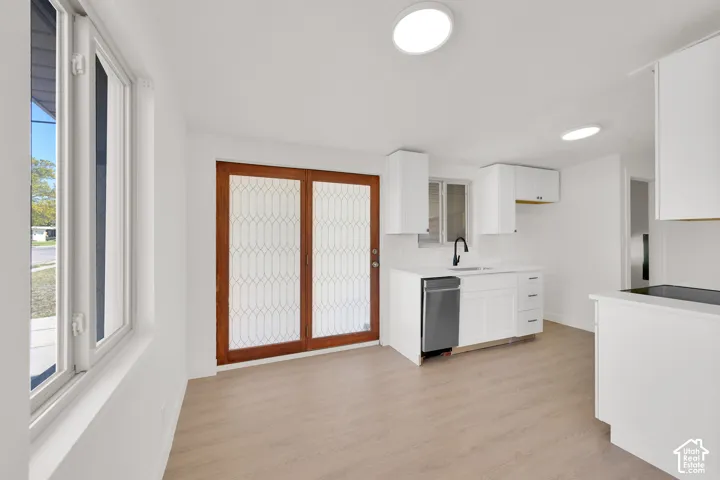 White kitchen cabinetry with black hardware, stainless steel dishwasher, wood-finish flooring, recessed lighting, and a glass-paneled door