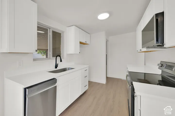 White shaker cabinetry with matte black hardware, stainless steel appliances, wood-finish flooring, and white countertops