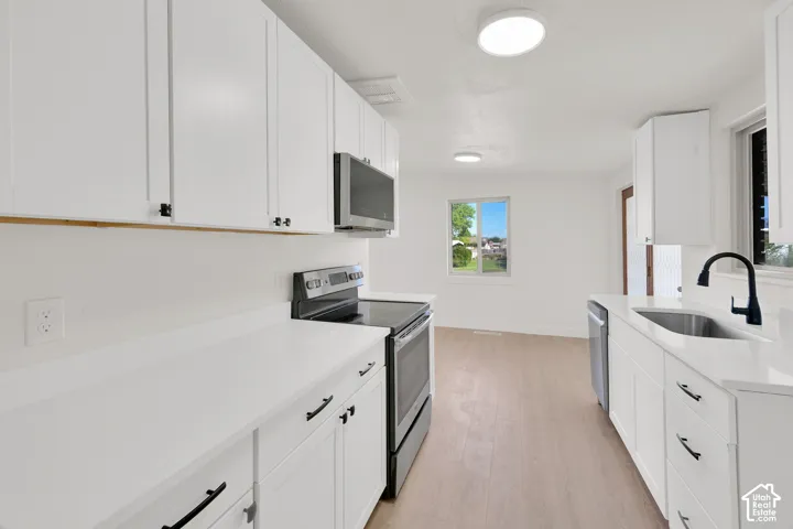 White shaker cabinetry with black hardware, stainless steel appliances, light wood-finish flooring, and white countertops
