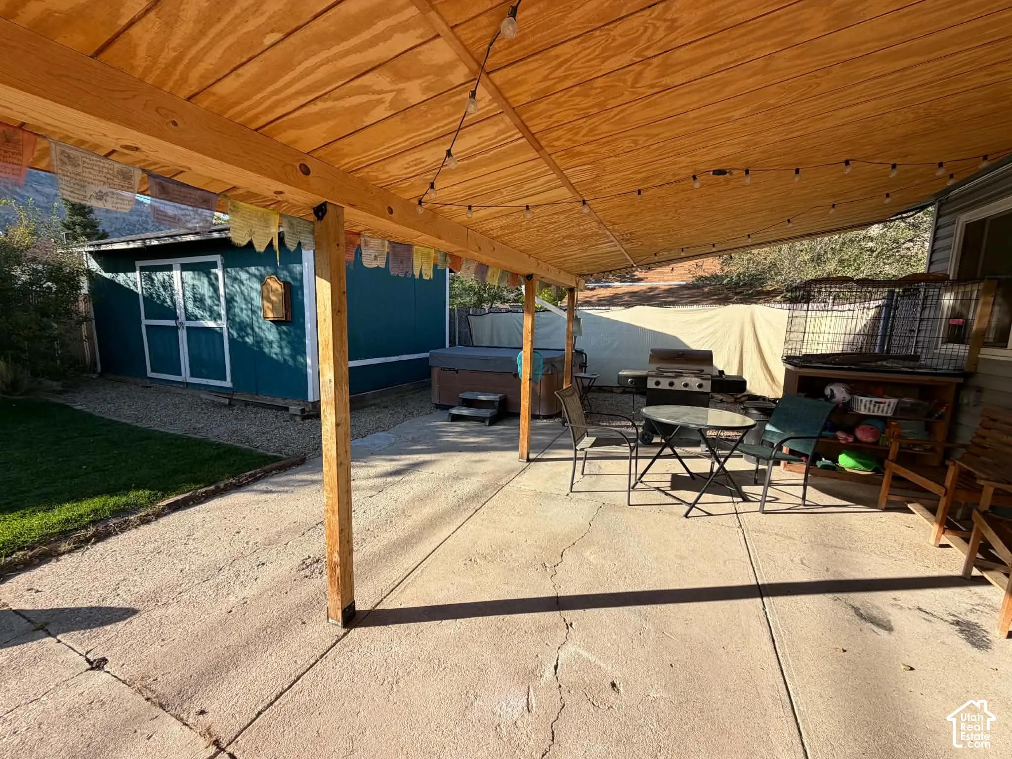 Covered concrete patio with string lighting, gravel landscaping, and a detached storage shed