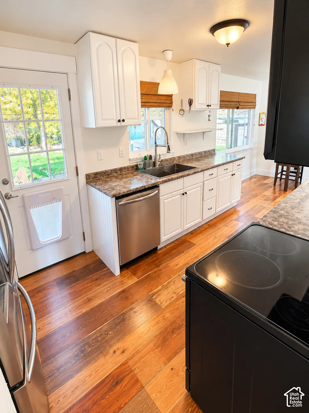 White cabinetry, wood-finish flooring, stainless steel dishwasher, integrated sink, and black electric range