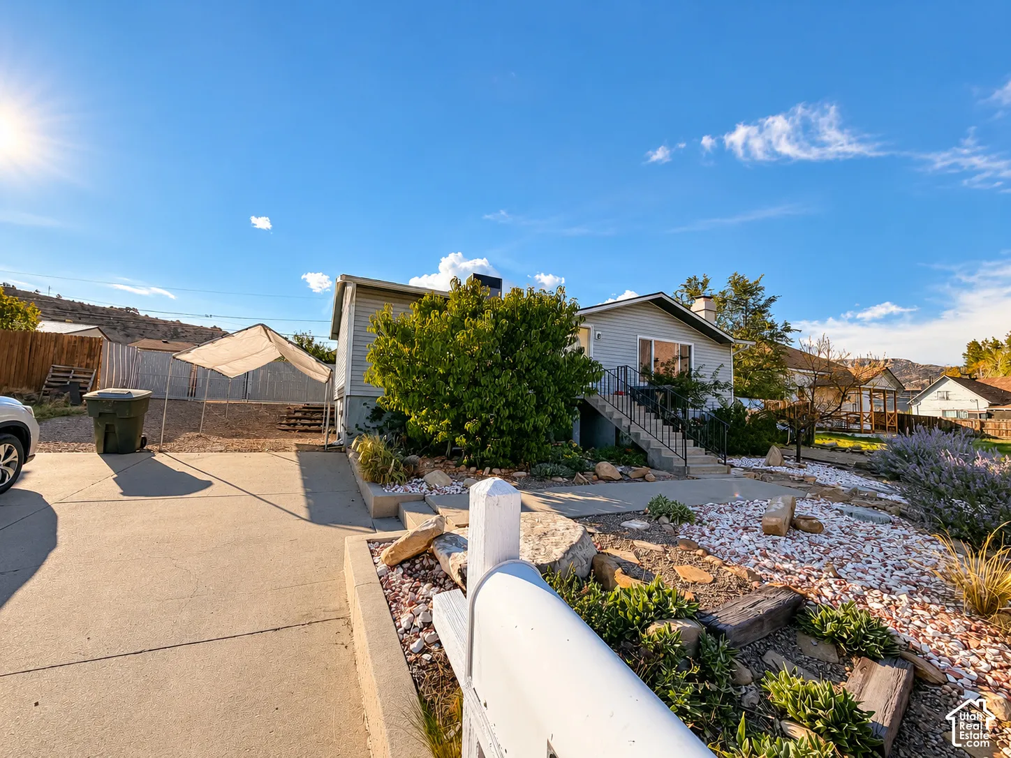 Concrete driveway, xeriscaped front yard with white gravel and plantings, built-in planters with wood accents, and a sloped front walkway with steps