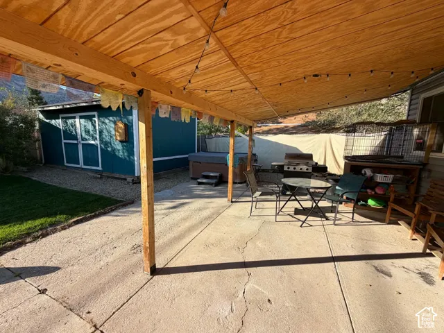 Covered concrete patio with string lighting, gravel landscaping, and a detached storage shed