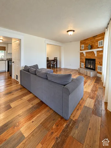 Spacious living area showcasing rich wood-finish flooring, a gas fireplace with built-in shelving and cabinetry, and an open layout connecting to the kitchen and dining spaces