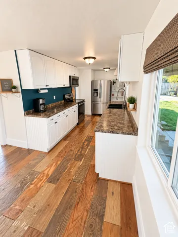Modern kitchen featuring white shaker cabinetry, granite countertops, stainless steel appliances including a French-door refrigerator, wood-finish flooring throughout, and a teal accent wall with pendant lighting and recessed ceiling fixtures