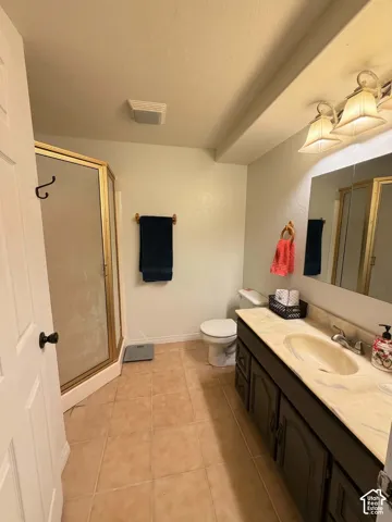 Tile flooring, vanity with integrated sink, gold-toned framed shower enclosure, recessed lighting, and wall-mounted light fixture