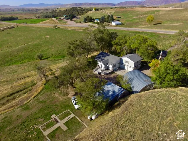 Two-story main residence with attached garage, expansive surrounding green spaces, and multiple outbuildings, all set against a mountain backdrop