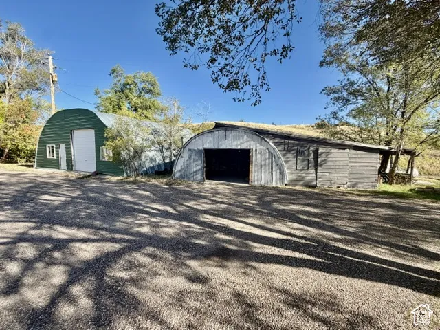 Two Quonset-style structures, one with a green metal exterior and a white overhead door, and another with a grey metal and wood exterior featuring an open bay