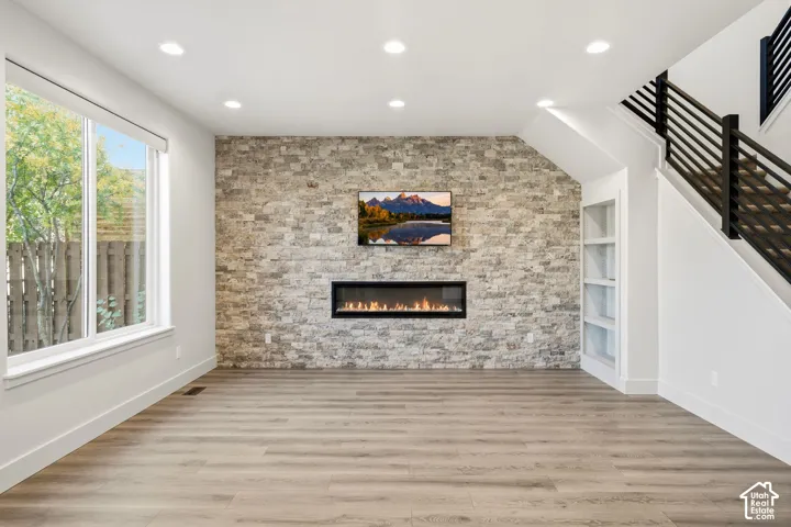 Wood-finish flooring, recessed lighting, expansive window, stone accent wall, and a built-in linear fireplace