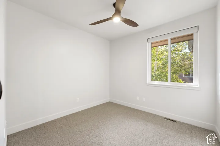 Neutral wall finishes with a single window, ceiling fan with integrated lighting, and carpet flooring