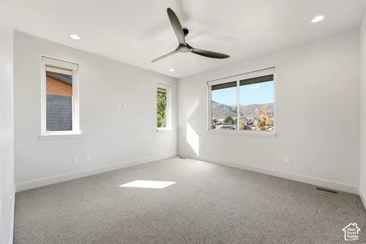 Recessed lighting, ceiling fan, multiple windows with roller shades, and gray carpeting