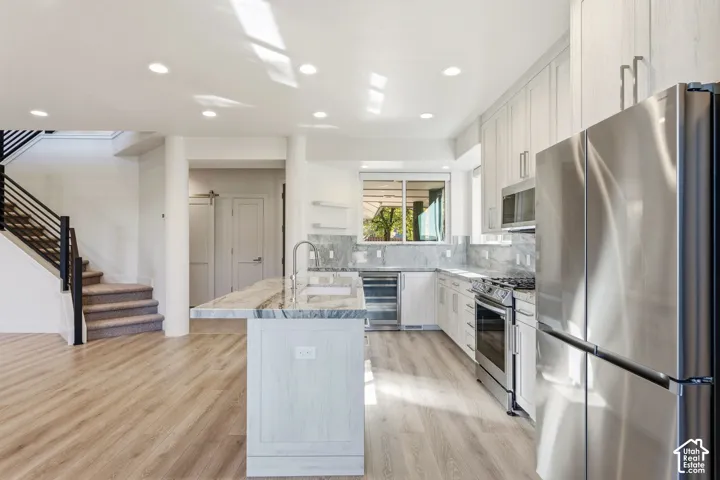 Gourmet kitchen featuring stainless steel appliances, light-toned cabinetry, and an island with a waterfall countertop