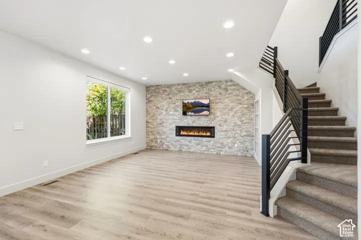 Expansive living area featuring wood-finish flooring, a stone-clad accent wall with a built-in linear fireplace, and recessed lighting