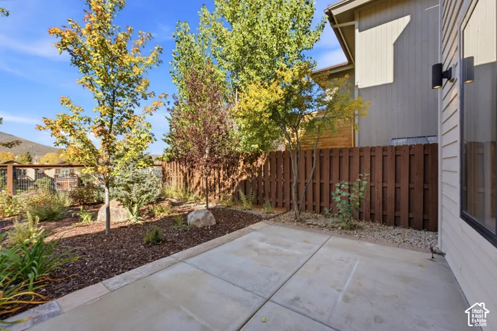Concrete patio with privacy fencing, mature trees, and landscaping with natural rock elements