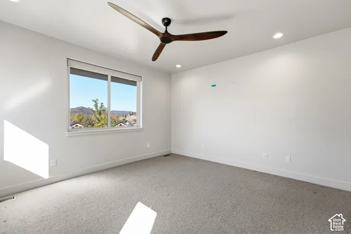 Recessed lighting, ceiling fan with wood-finish blades, and a large window with roller shades