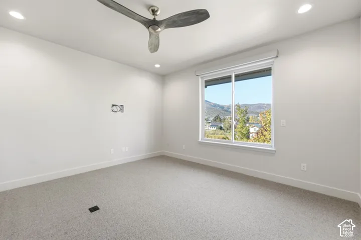 Spacious room featuring neutral carpeting, a modern ceiling fan, recessed lighting, and a large window with roller shades