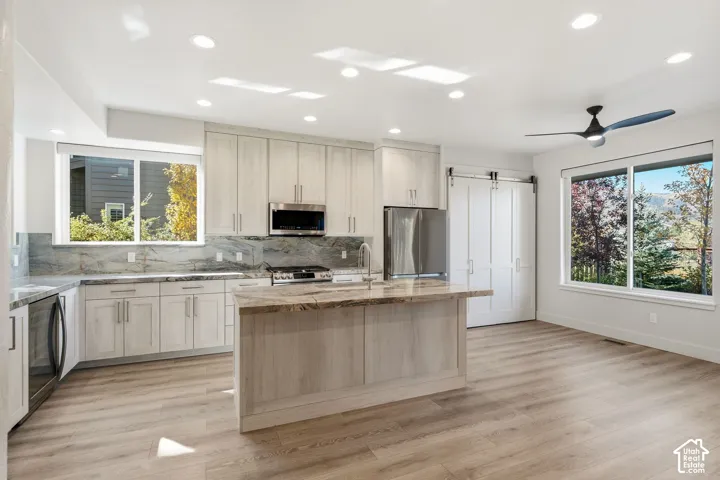Modern kitchen with light wood-finish cabinetry, stainless steel appliances, and an island with a stone countertop