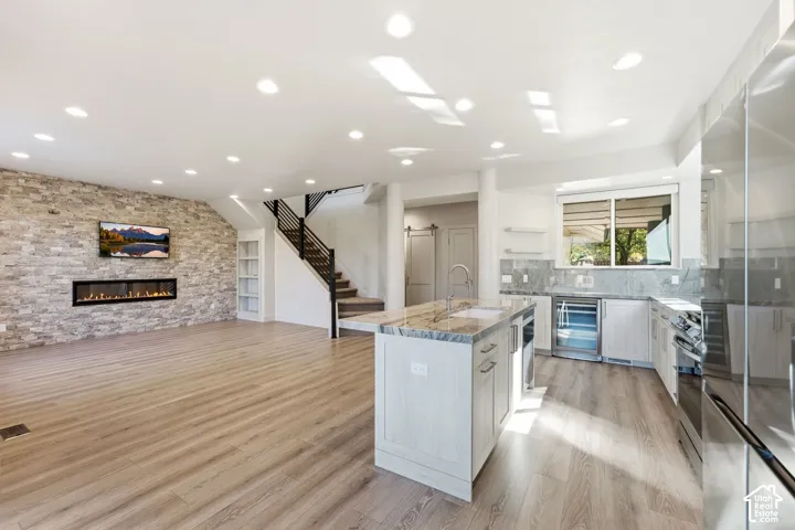 Open-concept living space featuring wood-finish flooring, a stone-clad accent wall with an electric fireplace, and a kitchen island with stone countertops