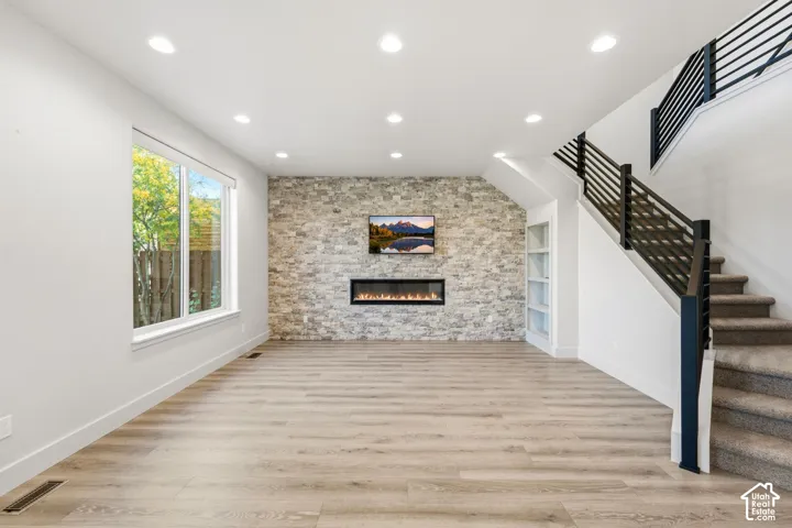 Recessed lighting, wood-finish flooring, stone accent wall, electric fireplace, and built-in shelving
