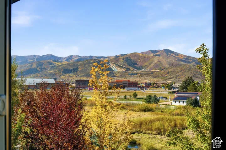 Expansive mountain backdrop with visible ski slopes, a verdant foreground, and a distant building with solar panels
