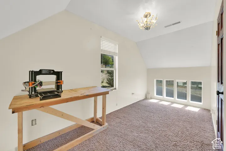 Vaulted ceiling with a decorative light fixture, multiple windows, and light-colored carpeting