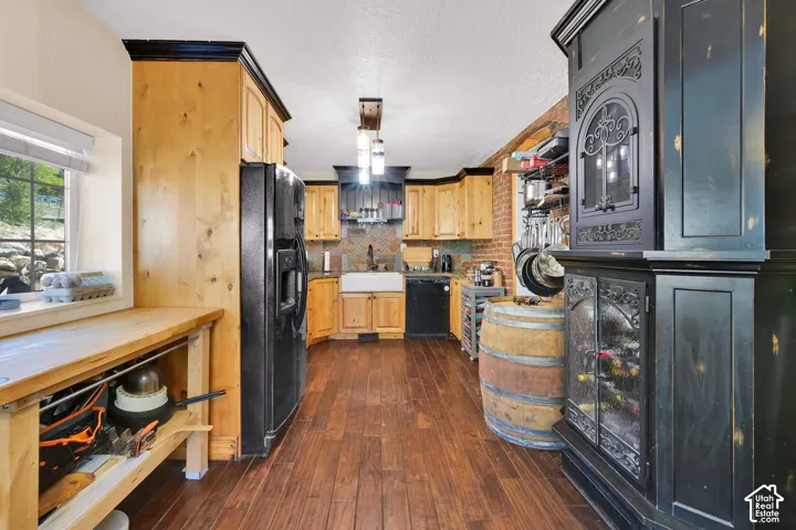 Wood-finish flooring, natural wood cabinetry with dark crown molding, a farmhouse-style sink, and a tiled backsplash