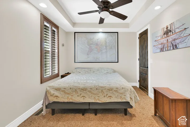 Tray ceiling with recessed lighting, ceiling fan, wood-finish window shutters, and a wood-finish door