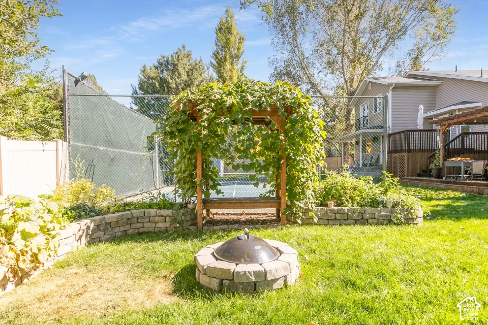 Expansive backyard featuring a stone-clad fire pit, a wooden arbor with climbing foliage, and a stone retaining wall defining garden beds