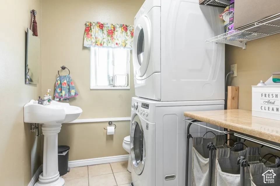 Pedestal sink, stacked laundry appliances, tiled flooring, built-in shelving, and countertop space