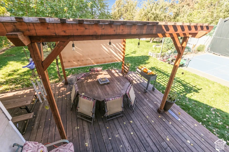 Expansive wooden deck with a built-in pergola, outdoor lighting, and a sports court