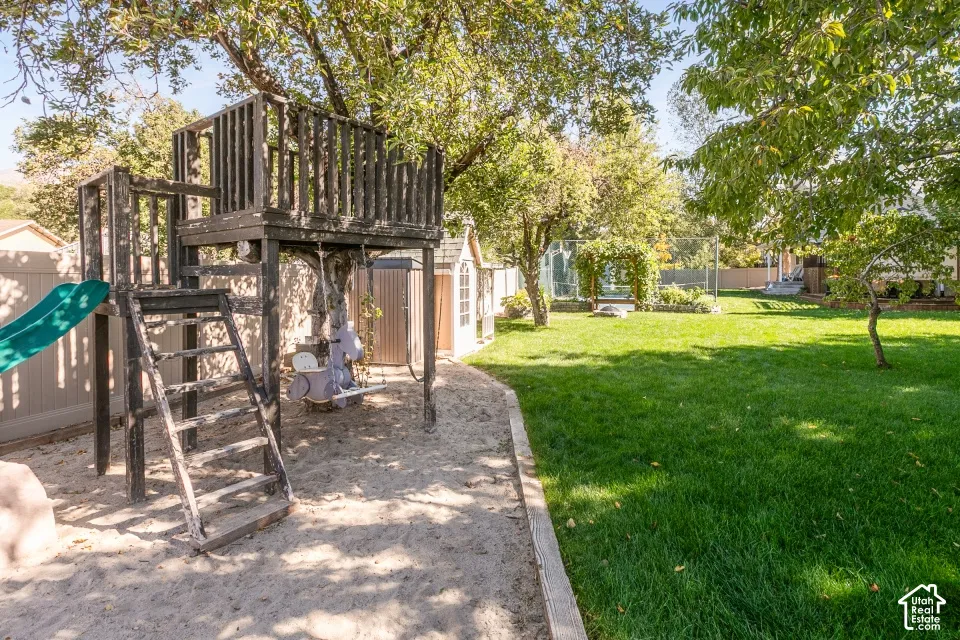 Expansive backyard featuring a manicured lawn, established trees, and a built-in play structure with a slide