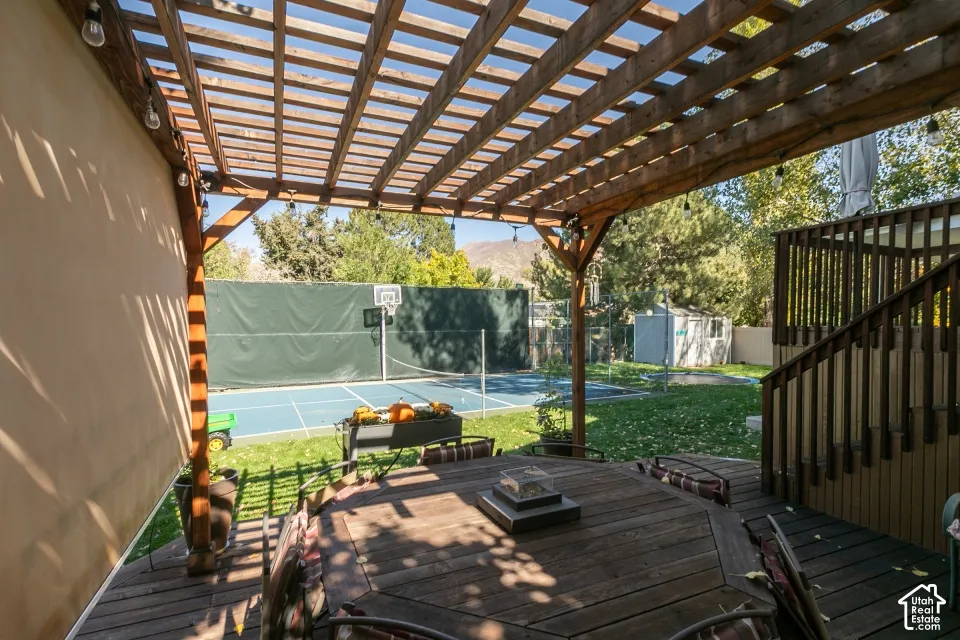 Expansive multi-level wood deck with a slatted pergola, overlooking a blue sport court
