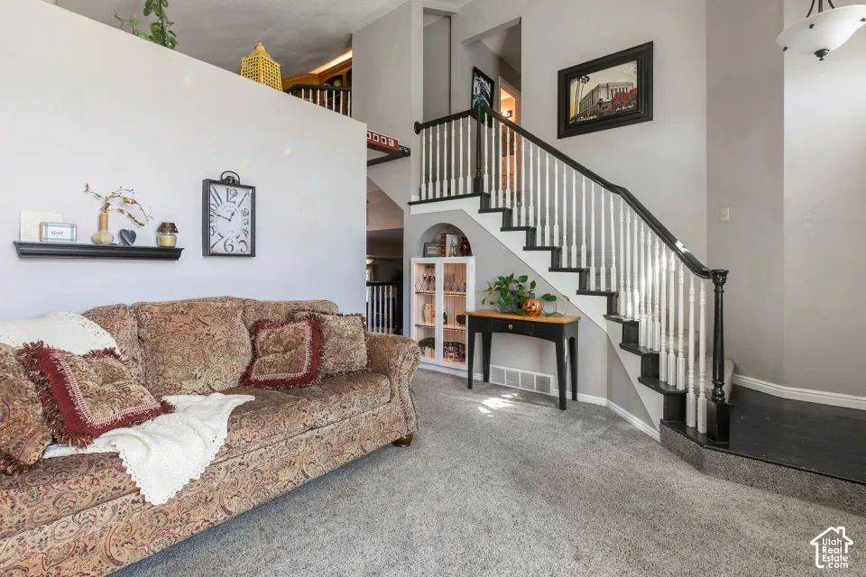 Carpeted flooring extending to the staircase, staircase with dark wood-finish handrail and balusters, built-in recessed archway with shelving, and a wall-mounted display shelf