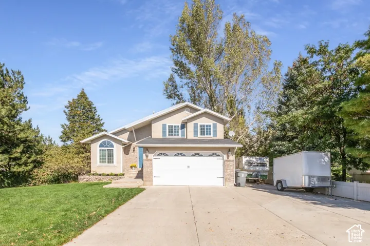 Stucco and brick exterior with a large concrete driveway, two-car garage, and mature landscaping