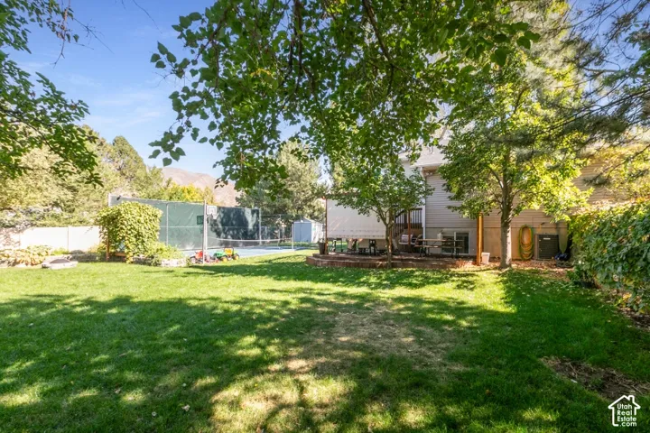 Expansive backyard featuring a sports court, mature trees, and a wooden deck