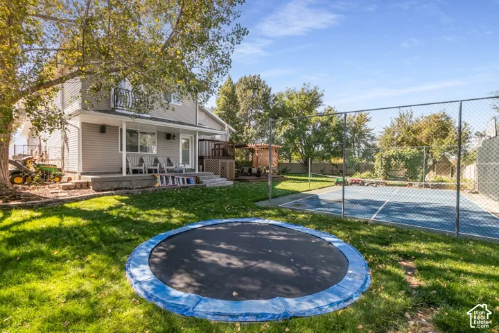 Expansive backyard featuring a manicured lawn, a built-in court with chain-link fencing, a multi-level deck, and mature trees