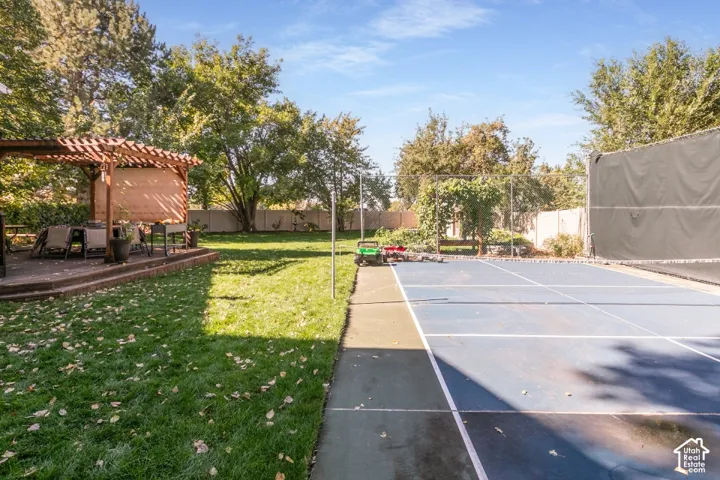 Expansive backyard featuring a manicured lawn, a raised patio with a wooden pergola, and a multi-sport court