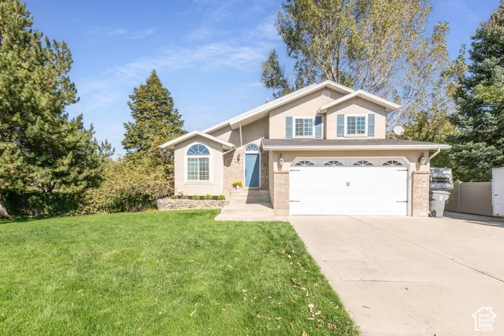 Two-story stucco exterior with a two-car garage, concrete driveway, and front lawn