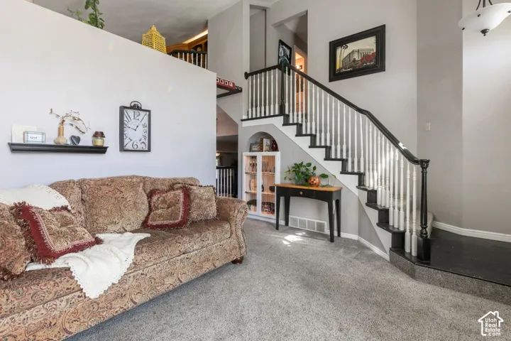 Carpeted flooring extending to the staircase, staircase with dark wood-finish handrail and balusters, built-in recessed archway with shelving, and a wall-mounted display shelf