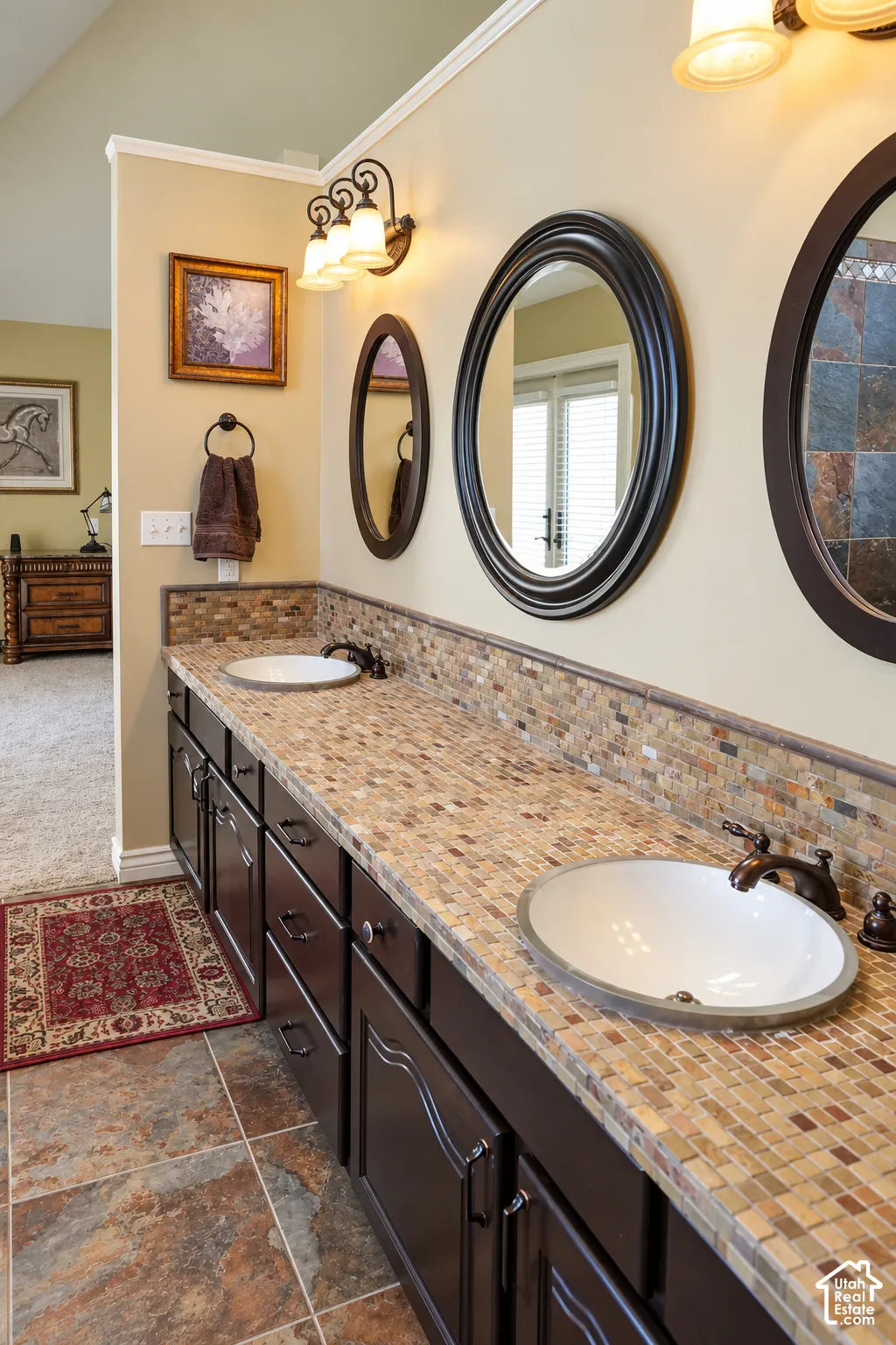 Spa-inspired dual vanity bathroom featuring paired round vessel sinks, dark cabinetry with ample storage, and tumbled stone tile countertops