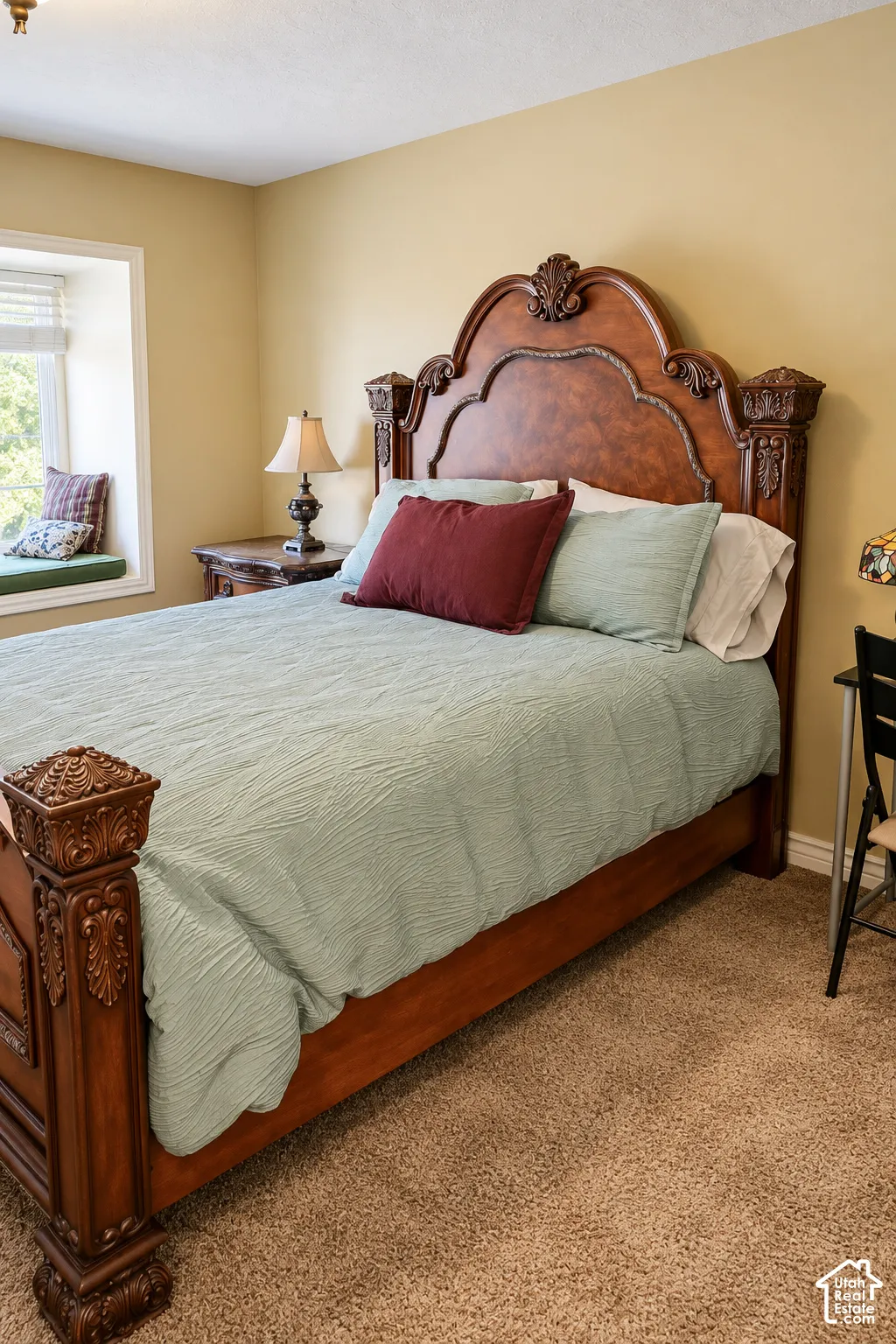 Elegant bedroom showcasing a carved wood bed frame with upholstered headboard, soft-close cabinetry, warm yellow walls, carpeted flooring, and abundant natural light from a large window